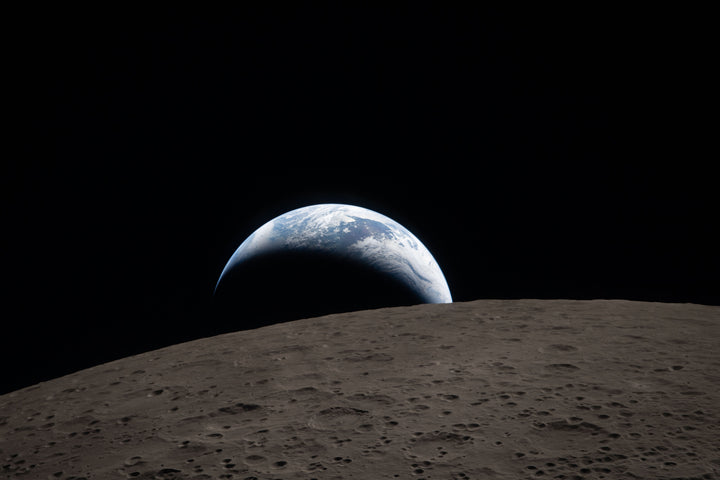 Earth, a muted blue sphere with bright white clouds, setting behind the cratered gray lunar surface as photographed by the Artemis II crew from the Orion spacecraft on April 6, 2026